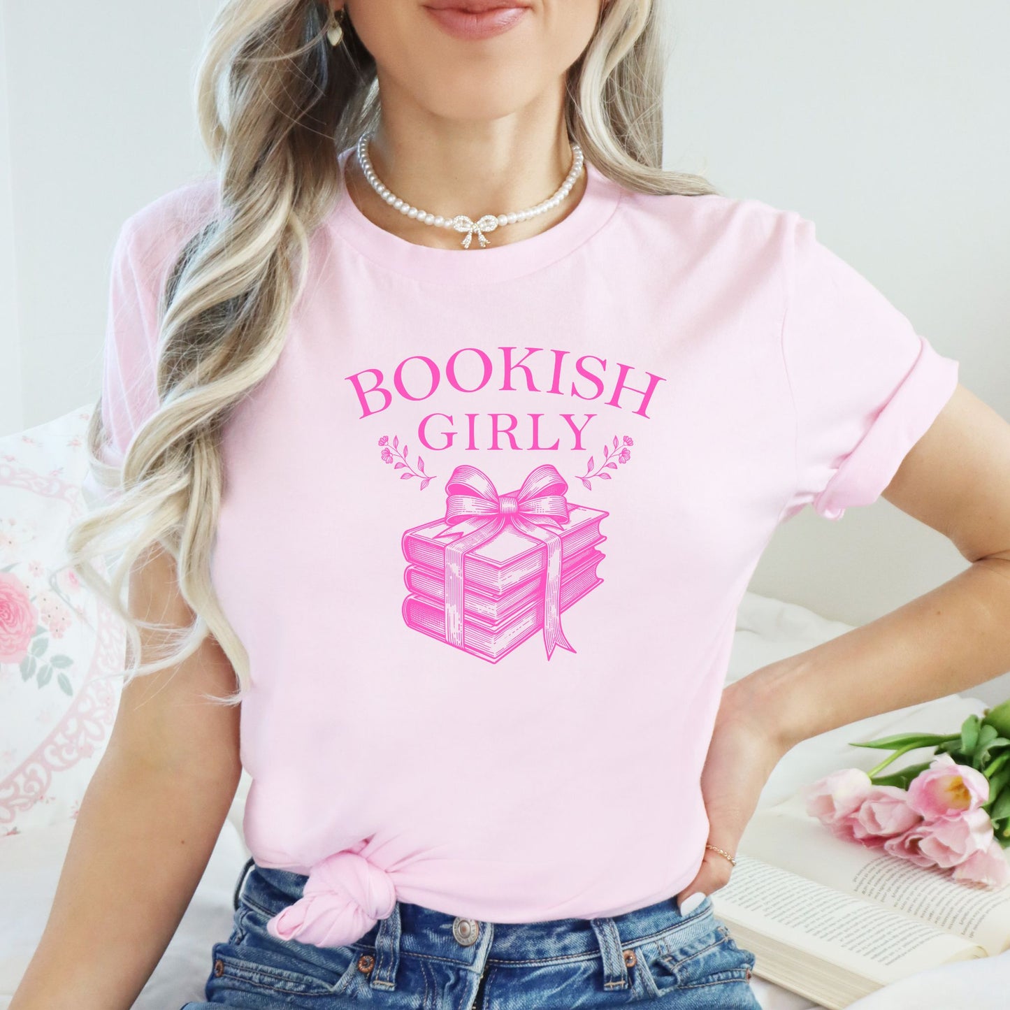 Person wearing a pink 'BOOKISH GIRLY' t-shirt with a stack of books design.