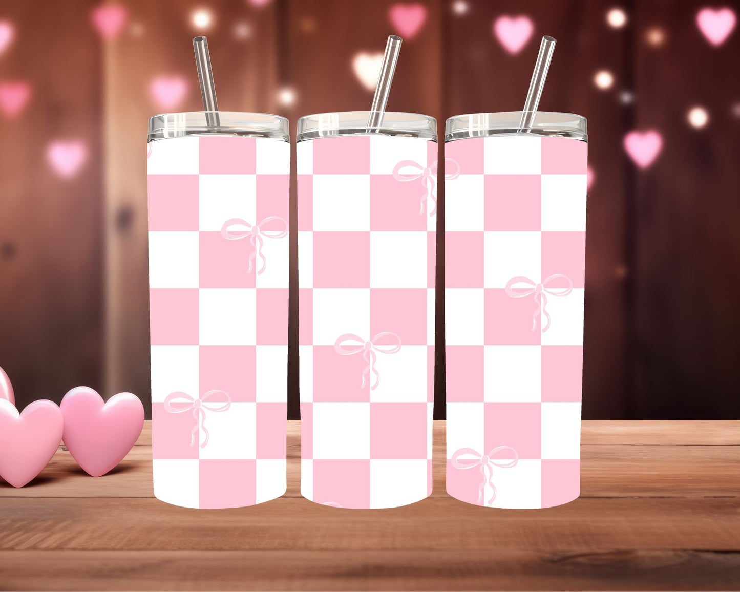 Three pink and white checkered tumblers with bow designs on a wooden surface.