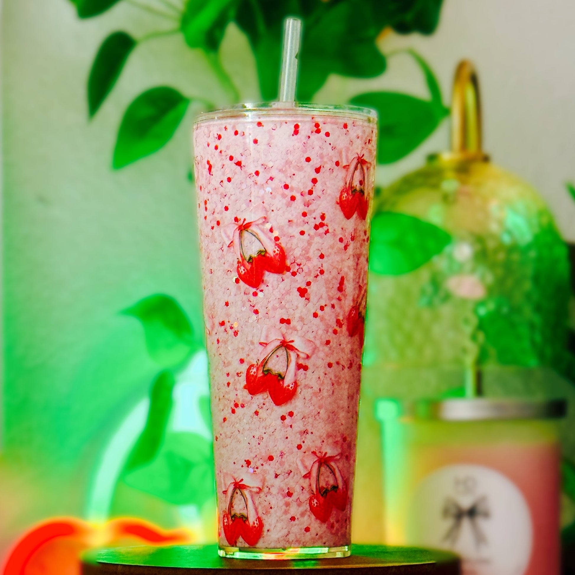 Custom cherry and bows pattern in a tall glass with a straw, against a green plant background.