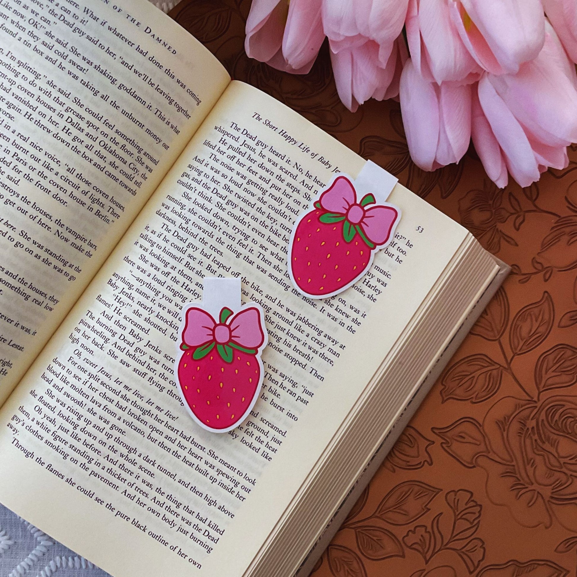 Two strawberry-shaped bookmarks with pink bows on an open book with pink flowers.