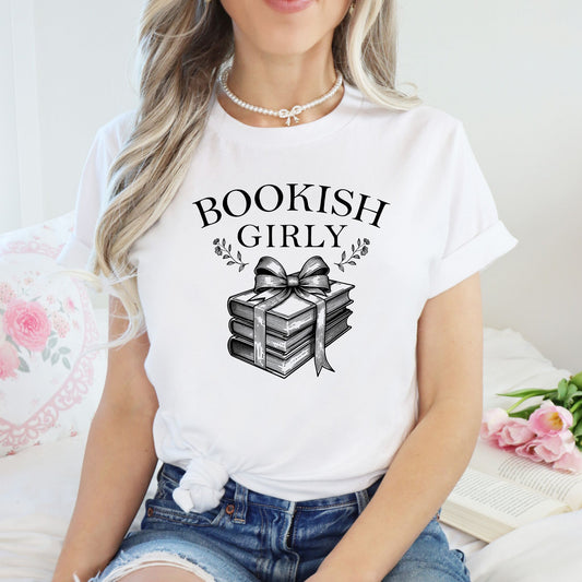 Person wearing a white t-shirt with 'BOOKISH GIRLY' design, sitting on a couch with flowers.
