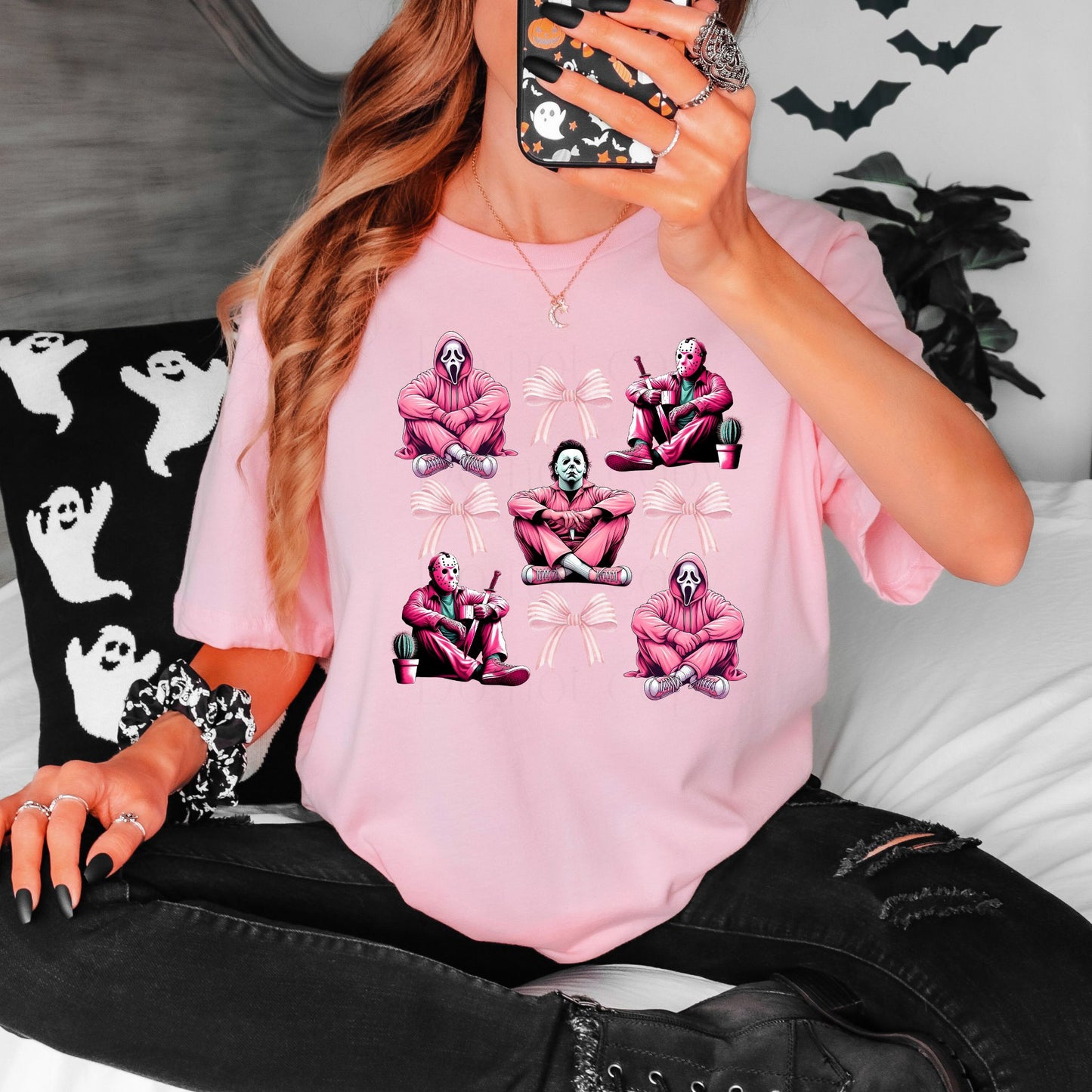 Person wearing a pink t-shirt with horror characters graphic designs, sitting on a bed 